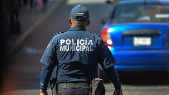 Ein Polizist der mexikanischen Policia municipal steht auf einer Straße, im Hintergrund parkt ein blaues Auto © picture alliance / NurPhoto | Artur Widak Foto: Artur Widak