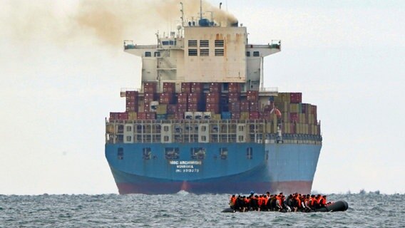 Eine Gruppe von Menschen, bei denen es sich vermutlich um Migranten handelt, überquert den Ärmelkanal in einem kleinen Boot von der französischen Küste aus in Richtung Dover. © Gareth Fuller/AP/dpa 