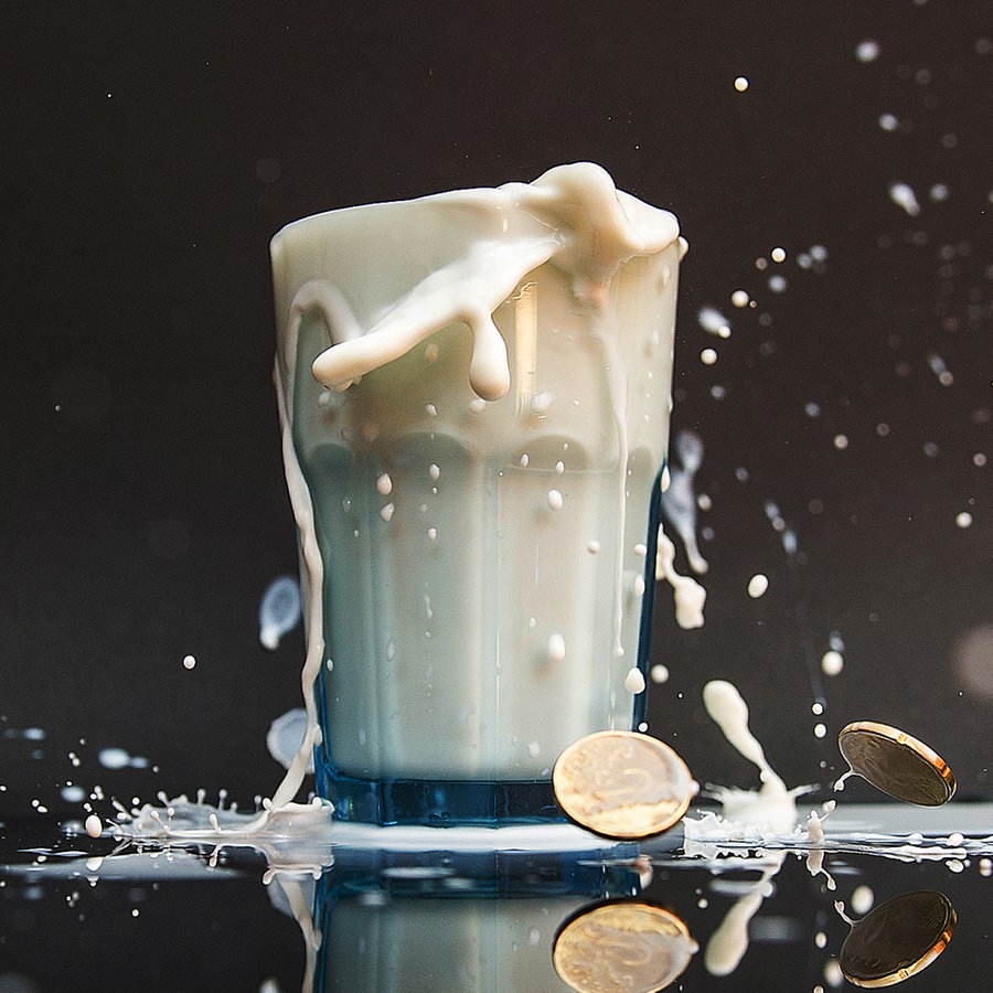 Ein Glas mit Milch, die über den Rand hinausläuft und einige Euro Geldstücke liegen auf dem Boden © picture alliance / dpa Foto: Paul Zinken