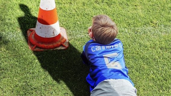 Bedrohlicher Schatten eines Erwachsenen fällt auf einen Jungen, der am Spielfeldrand sitzt (Bildmontage) © imago/blickwinkel 