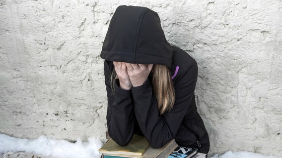 Ein trauriges Kind sitzt mit Schulbüchern auf dem Schoß an einer Wand © imago images Foto: Andreas Weihs