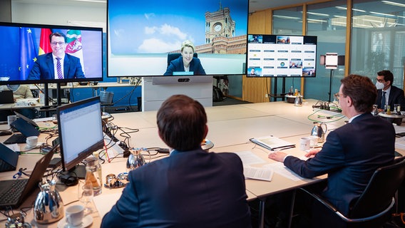 NRW-Ministerpräsident Hendrik Wüst (CDU, r.) sitzt bei einer Videokonferenz an einem Tisch und vor mehreren Monitoren. © dpa bildfunk Foto: Bernd von Jutrczenka