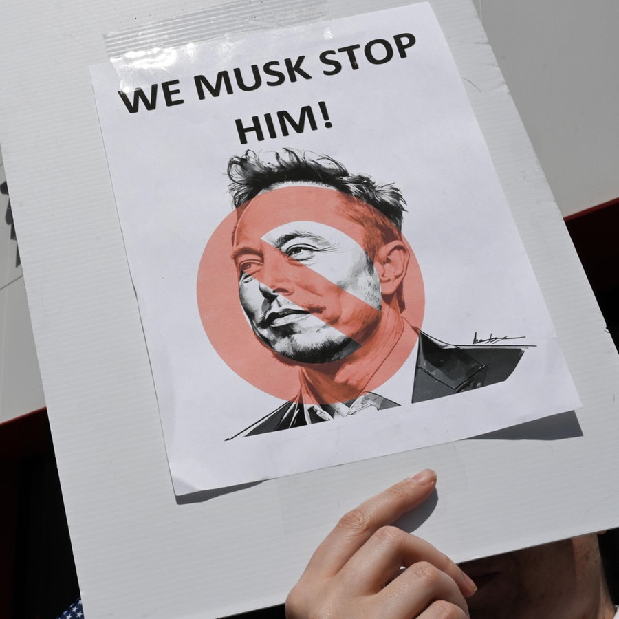 Auf einer Demonstration gegen Elon Musk / Tesla in den USA hält ein Protestant ein Schild mit der Aufschrift "WE MUSK STOP HIM!" hoch © picture alliance / Anadolu Foto: Tayfun Coskun