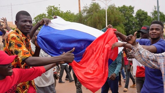 Anhänger des Militärs feiern den Putsch und halten dabei eine russische Flagge hoch © dpa/AP | Sam Mednick Foto: Sam Mednick