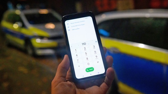 Die Notrufnummer "110" ist auf einem Smartphone eingegeben, dass vor zwei Streifenwagen gehalten wird. © picture alliance Foto: Jonas Walzberg