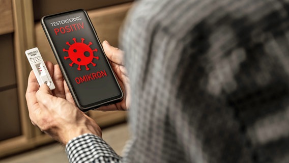 A man is holding a smartphone and a positive rapid test for coronavirus.  The black display of the smartphone reads in red: Positive Omikron test result.  © picture alliance / CHROMORANGE |  Michael Bihlmeyer 