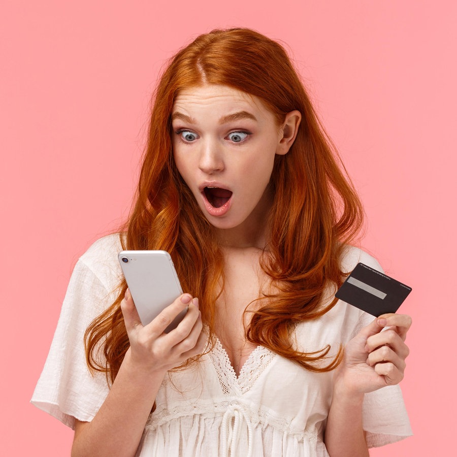 Junges Mädchen schaut schockiert auf ihr Smartphone, das sie in der linken Hand hält, in der rechten Hand hält sie eine Creditkarte © picture alliance / Zoonar Foto: Seva Levitsky
