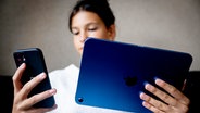 Ein Mädchen schaut auf ein Tablet und auf ein Smartphone © picture alliance 