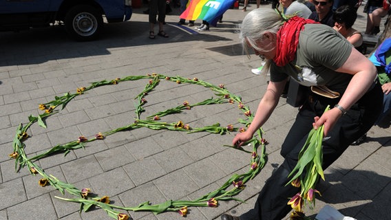 Eine Frau legt bei einem Ostermarsch mit Tulpen das Friedenszeichen auf den Bürgersteig. © dpa Foto: Angelika Warmuth