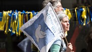 Das Symbol der "Friedenstaube" auf einer Fahne einer Frau bei einem Ostermarsch 2023. © picture alliance Foto: Sebastian Gollnow