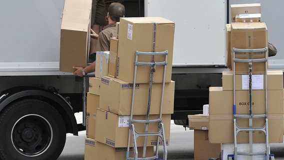 Zwei Sackkarren mit vielen Paketen stehen vor einem weißen Transporter während ein Paketzusteller die Pakete einlädt. © dpa Foto: Frank Hoermann