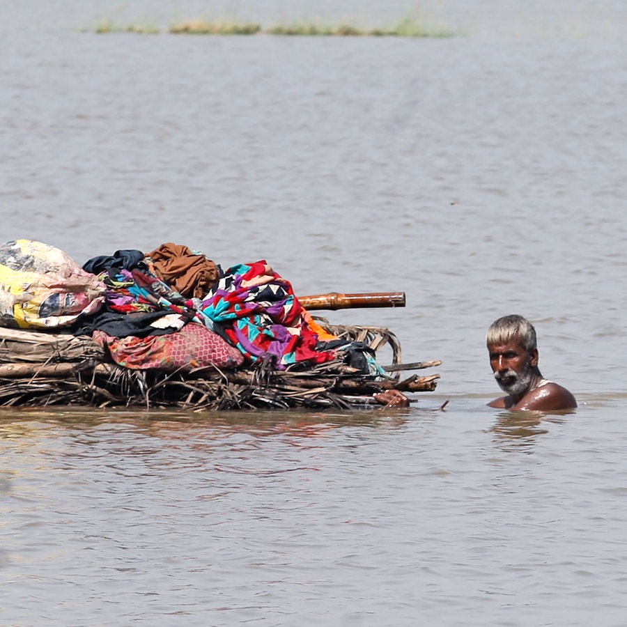 Ein Mann schwimmt im Wasser, vor ihm ein Floß mit Habseligkeiten. © dpa-Bildfunk Foto: Fareed Khan/AP/dpa