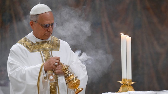Der Papst Leo XIV. feiert seine erste Messe in seinem neuen Amt in der Sixtinischen Kapelle und schwingt ein goldenes Weihrauchfass aus dem racuh aufsteigt. © Uncredited/Vatican media/AP/dpa 