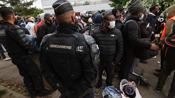 Nach der Räumung eines besetzten Hauses in Paris stehen Polizisten und obdachlose Migranten auf der Straße. © AFP/dpa Foto: Emmanuel Dunand