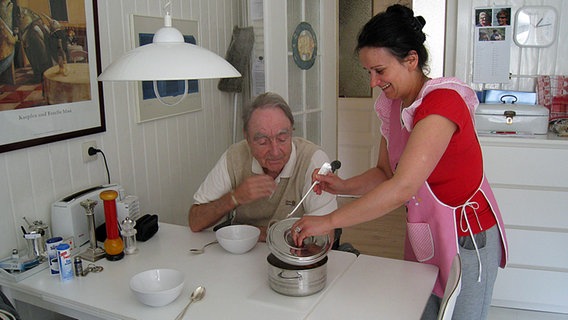Eine Pflegerin serviert einem am Tisch sitzenden älteren Mann das Essen. © NDR Foto: Bettina Less