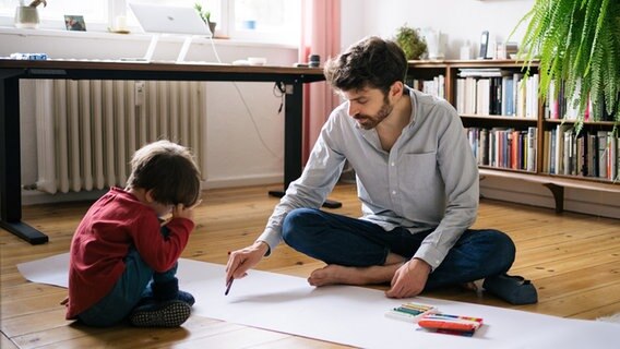 Ein Mann sitzt neben seinem Sohn auf dem Boden des Zimmers © Marcus Heep Foto: Marcus Heep