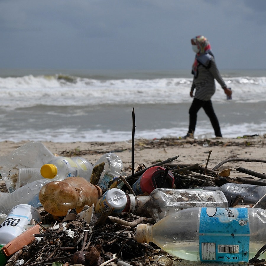Eine Frau geht an einem Strand entlang, an dem Plastikmüll angespült wurde. © picture alliance/dpa/BERNAMA Foto: Mohd Khairul Fikiri Osman