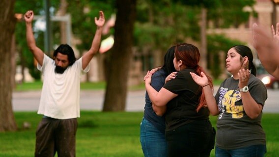 Auf einer Wiese nehmen sich zwei Frauen in den Arm und trösten einander © picture alliance/dpa/The San Antonio Express-News/AP | Billy Calzada Foto: Billy Calzada