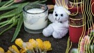 Blumen, Kerzen und ein Teddybär liegen und stehen im Stadtteil Alsterdorf vor dem Eingang zu einer Kirche der Zeugen Jehovas. In dem Raum hatte es zuvor einen Amoklauf gegeben, bei dem mehrere Menschen getötet wurden. © picture alliance Foto: Daniel Bockwoldt