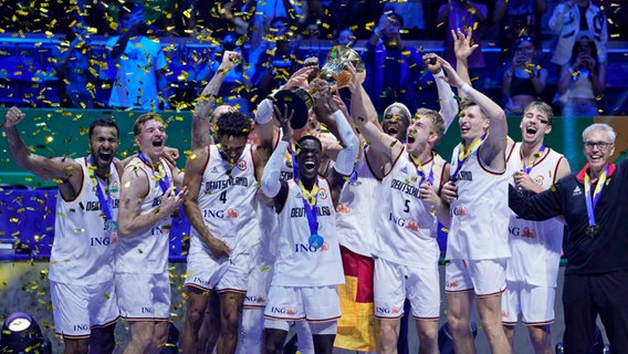 Das deutsche Team jubelt mit der Trophäe über den Sieg bei der Basketball-WM 2023. © AP/dpa Foto: Michael Conroy
