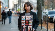 Shira Havron hält ein Plakat mit Fotos von ihren Angehörigen, die von der Terrororganisation Hamas als Geiseln genommen wurden. Angehörige von deutschen Geiseln im Gazastreifen haben die Bundesregierung erneut um Hilfe für deren Freilassung gebeten. © picture alliance/dpa Foto: Christophe Gateau