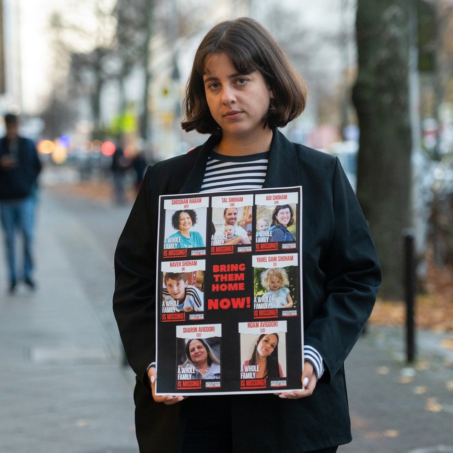 Shira Havron hält ein Plakat mit Fotos von ihren Angehörigen, die von der Terrororganisation Hamas als Geiseln genommen wurden. Angehörige von deutschen Geiseln im Gazastreifen haben die Bundesregierung erneut um Hilfe für deren Freilassung gebeten. © picture alliance/dpa Foto: Christophe Gateau
