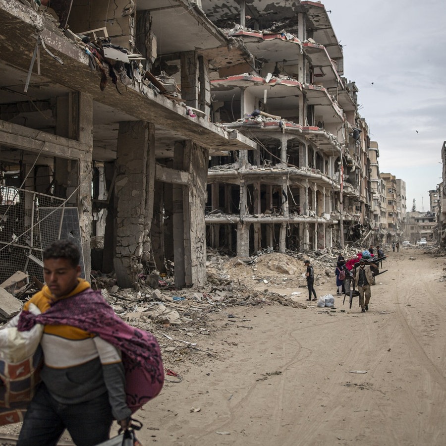 Menschen gehen durch eine Straße in Khan yunis, Gaza, mit durch Bomben zerstörten Wohnhäusern © picture alliance / Anadolu Foto: Jehad Alshrafi