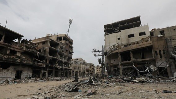 Menschen gehen durch eine Straße in Khan yunis, Gaza, mit durch Bomben zerstörten Wohnhäusern © picture alliance / ZUMAPRESS.com | Foto: Omar Ashtawy