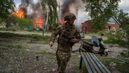 Ein Polizist läuft vor einem brennenden Haus, das durch einen russischen Luftangriff zerstört wurde. © picture alliance/dpa/AP | Evgeniy Maloletka Foto: Evgeniy Maloletka