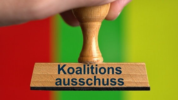 Ein symbolischer Holzstempel mit der Aufschrift "Koalitionsausschuss", gehalten von einer Hand, vor den Farben der Ampel-Koalition. © picture alliance / SULUPRESS.DE | Torsten Sukrow / SULUPRESS.DE Foto:  Torsten Sukrow / SULUPRESS.DE