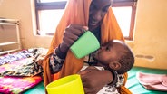 Eine Frau füttert ein Baby mit einem Becher. © NDR / Zeitenspiegel / Rainer Kwiotek Foto: Rainer Kwiotek