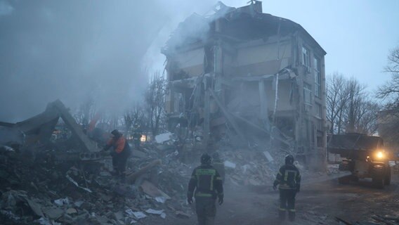 Rauch steigt aus den Trümmern eines durch Beschuss zerstörten Einkaufszentrums in Donezk (Ukraine) auf, während Feuerwehrleute im Einsatz sind. © AP/dpa Foto: Alexei Alexandrov