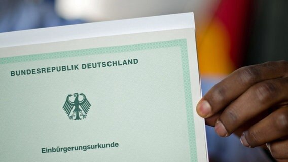 Ein Mann aus Afrika hält seine Einbürgerungsurkunde der Bundesrepublik Deutschland in der Hand. © dpa Foto: Julian Stratenschulte