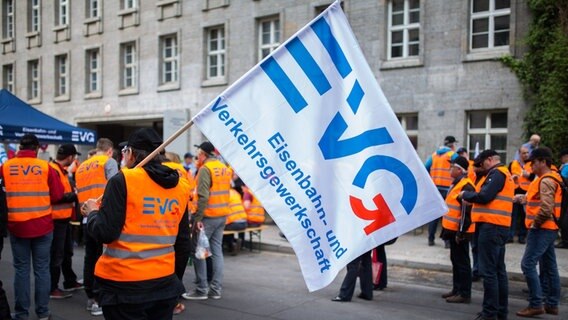 Mitglieder der Eisenbahn- und Verkehrsgewerkschaft (EVG) nehmen an einer Kundgebung teil und schwenken Fahnen. © picture alliance / dpa Foto: Lukas Schulze
