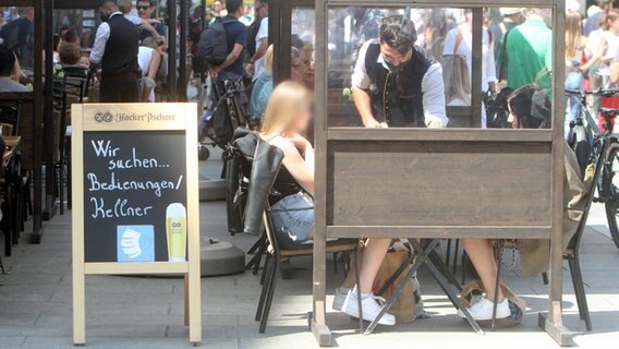 Ein Aufsteller mit Aufschrift "Wir suchen Bedienungen / Kellner" steht vor einem Restaurant in der Innenstadt von München. © imago images 0131374343h Foto: Ralph Peters