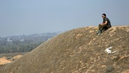 Ein israelischer Soldat sitzt auf einer Anhöhe nahe der Grenze zum Gazastreifen im Süden Israels. © AP/dpa Foto: Tsafrir Abayov