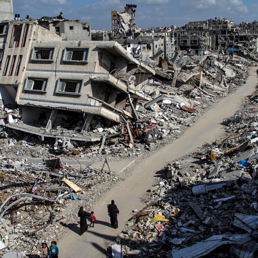 Menschen gehen an den Ruinen von Gebäuden in Dschabalia im Gazastreifen vorbei. © dpa Foto: Mahmoud Issa
