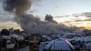 Hinter einem Zeltlager für vertriebene Palästinenser in Gaza-Stadt steigt Rauch aus einem Gebäude auf, das von der israelischen Armee angegriffen wurde. © AP/dpa Foto: Jehad Alshrafi