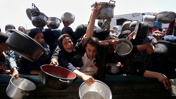 Palästinenser ringen mit Töpfen in der Hand um gespendete Lebensmittel in einer Gemeinschaftsküche in Khan Younis (Gazastreifen). © AP/dpa Foto: Abdel Kareem Hana