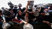 Palästinenser ringen mit Töpfen in der Hand um gespendete Lebensmittel in einer Gemeinschaftsküche in Khan Younis (Gazastreifen). © AP/dpa Foto: Abdel Kareem Hana