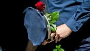 Ein Polizist hält bei einem Gedenken am Ende eines Schweigemarschs der "Blaulichtfamilie" von der Deutschen Polizeigewerkschaft (DPolG) und der Gewerkschaft der Polizei (GdP) für den durch einen Messerangriff in Mannheim zu Tode gekommenen Polizisten eine Rose. © dpa Foto: Christoph Soeder