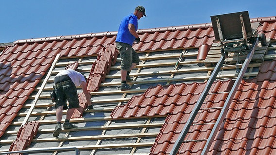 Zwei Dachdecker stehen auf dem First eines ungedeckten Daches. © NDR Foto: Axel Franz