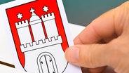 Stimmzettel mit Hamburg-Wappen wird in eine Wahlurne geworfen, Symbolfoto Bürgerschaftswahl in Hamburg. © picture alliance Foto: Christian Ohde