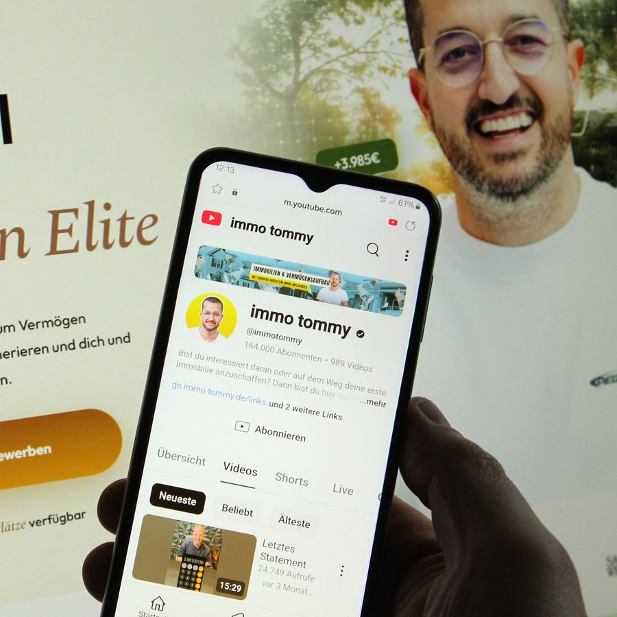 Auf einem Laptop sieht man die Website vom Influencer "Immo Tommy", davor zeigt ein Handy seinen YouTube-Kanal. © imago Foto: Hanno Bode