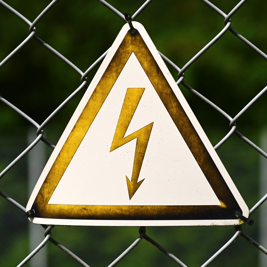Schild mit Strompfeil an einem Zaun. © picture alliance Foto: Christian Ohde