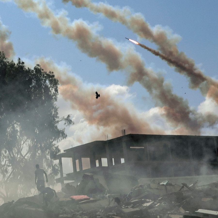Raketen aus dem Gazastreifen werden über zerstörte Gebäude hinweg auf Israel abgefeuert. © AP/dpa Foto: Mohammed Dahman