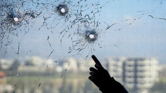 Jemand zeigt auf Einschusslöcher in einem Fenster in der Stadt Jableh in der Provinz Latakia im Nordwesten Syriens. © AP/dpa Foto: Omar Albam