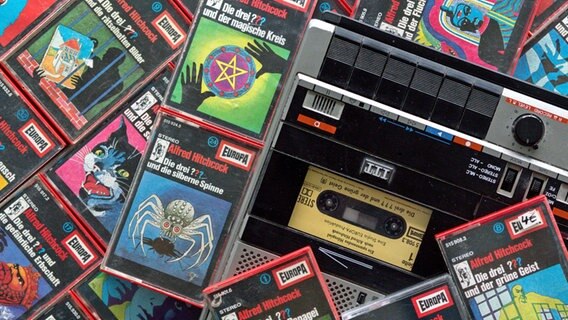 Zahlreiche Kassetten der Hörspielserie «Die drei Fragezeichen» liegen neben einem Kassettenrekorder. © picture alliance/dpa Foto: Wolfram Kastl