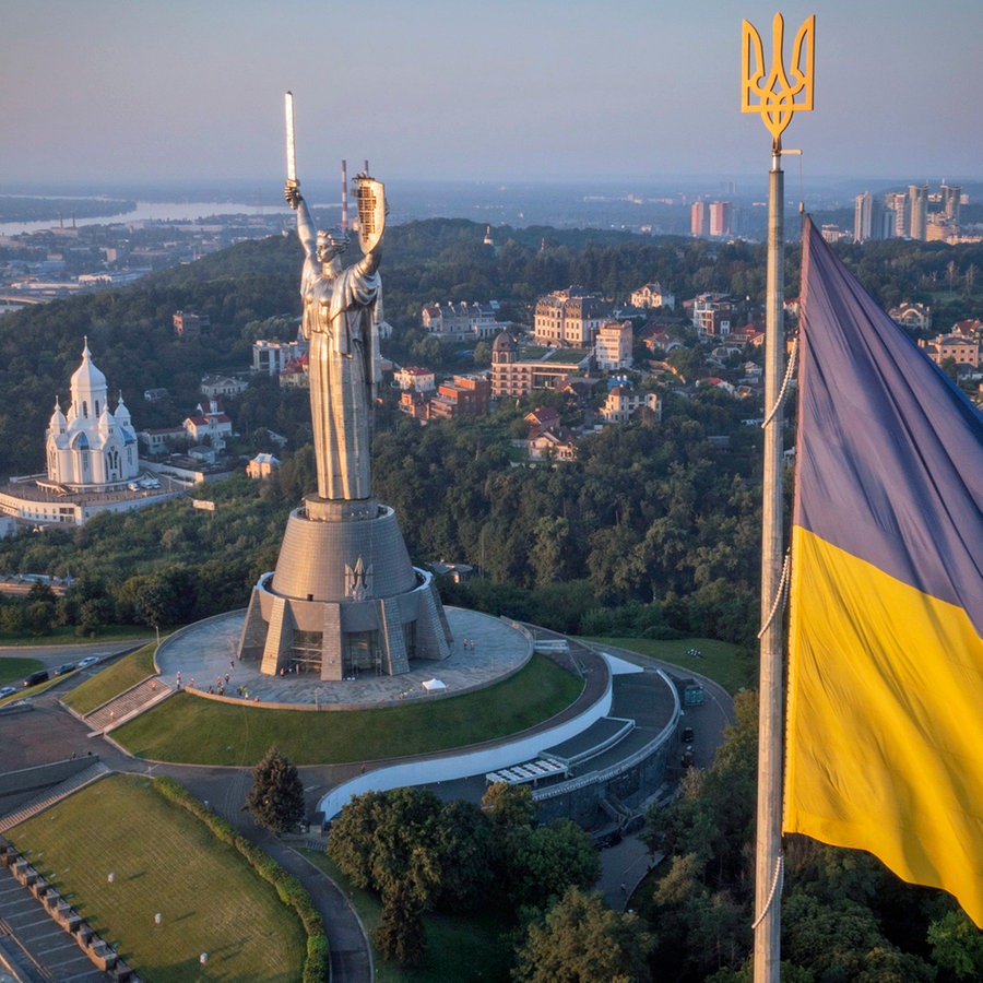 Die ukrainische Nationalflagge weht, während Arbeiter das ukrainische Wappen auf das Schild in der Hand des Mutterland-Denkmals montieren, nachdem ein Staatswappen der Sowjetunion vom Schild entfernt worden ist. © AP/dpa Foto: Efrem Lukatsky