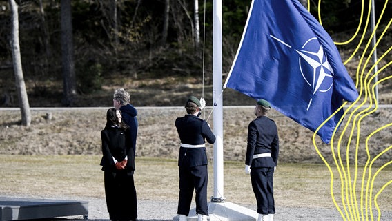 Der schwedische Justizminister Gunnar Strömmer und die Klimaministerin Romina Pourmokhtari nehmen an der Zeremonie teil, bei der am Montag, dem 11. März, die NATO-Flagge auf dem Marinestützpunkt Musko außerhalb von Stockholm gehisst wird. © picture alliance / TT NEWS AGENCY | Fredrik Sandberg/TT Foto: Fredrik Sandberg